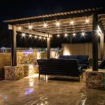 A resort style backyard at night with a waterfall, pergola, and a firepit at night.