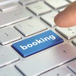 A finger about to press a blue button with the word "booking" written on it to imply that the person is booking a vacation rental.