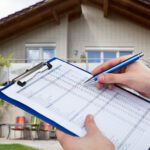 Vacation rental property inspection - a pair of hands holding a blue clipboard and pen in front of a house