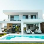 A white home with a pool and sun chairs.