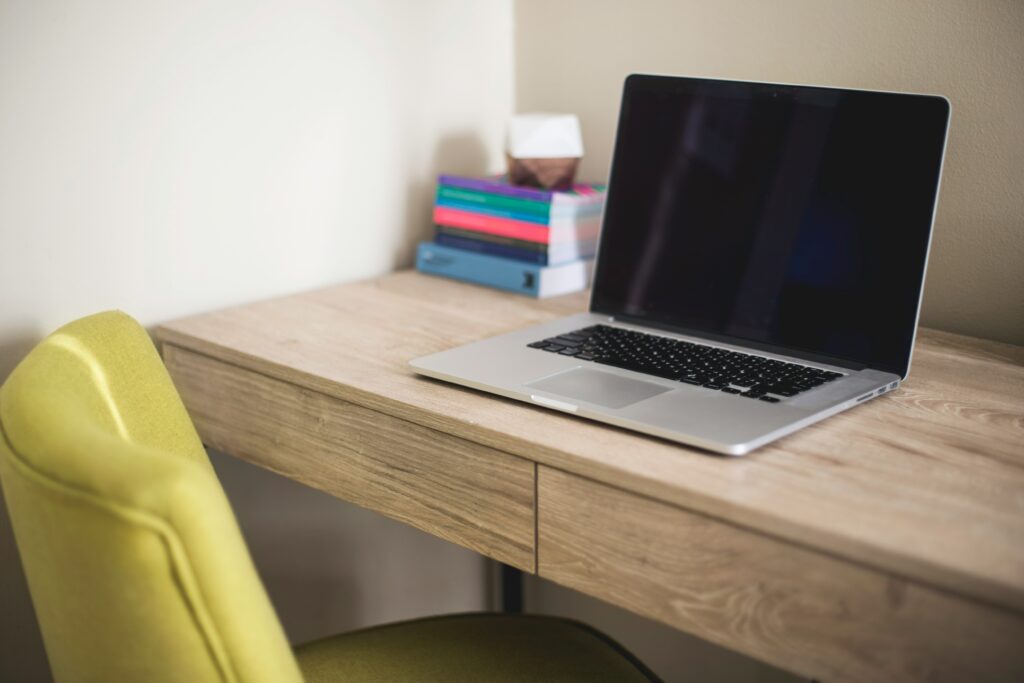 Um laptop em uma mesa com uma cadeira verde.